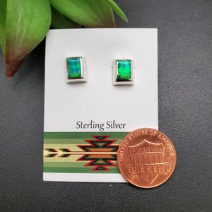 May include: A pair of sterling silver earrings with green opal stones. The earrings are displayed on a white card with the words "Sterling Silver" printed on it. A penny is included for size reference.