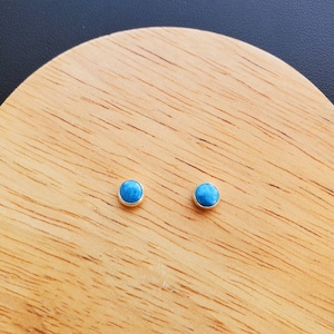 May include: A pair of small, round, blue gemstone earrings on a wooden surface.