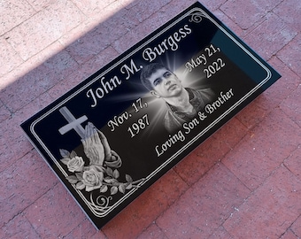 May include: Black granite memorial plaque with a silver inscription and a photo of a young man. The inscription reads "John M. Burgess, Nov. 17, 1987 - May 21, 2022, Loving Son & Brother".