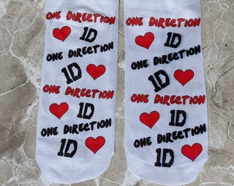 Op de afbeelding: Een paar witte sokken met een rood hart en de tekst "ONE DIRECTION" en "1D" die op elke sok wordt herhaald.
