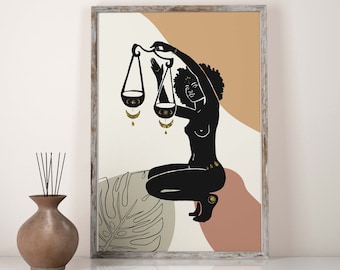 May include: A framed art print featuring a black silhouette of a person holding scales, with gold accents. The artwork has a neutral color palette with beige, brown, and peach tones. A decorative vase with reeds is in the foreground.