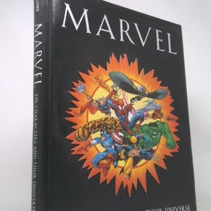 May include: A hardcover book titled "MARVEL" with a black cover. The cover features a colorful illustration of various Marvel characters within a burst of orange and yellow. The spine reads "MARVEL THE CHARACTERS AND THEIR UNIVERSE."