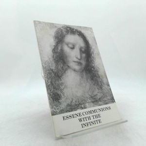 May include: A book titled "Essene Communions With The Infinite" is displayed on a clear stand. The book cover features a grayscale portrait of a person with long hair and closed eyes. The book is set against a white background.