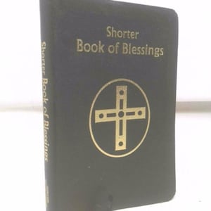 May include: A black book titled "Shorter Book of Blessings" with gold lettering and a gold cross emblem. The book has a yellow ribbon bookmark.