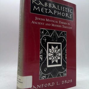 May include: A hardcover book titled "Kabbalistic Metaphors" with the subtitle "Jewish Mystical Themes in Ancient and Modern Thought." The cover is a deep red with black and white geometric designs and text. The author's name, Sanford L. Drob, is printed at the bottom.