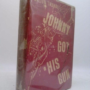 May include: A vintage hardcover book titled "Johnny Got His Gun" by Dalton Trumbo. The book has a red cover with a faded illustration and text. The book is wrapped in clear plastic.