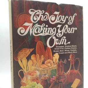 May include: A vintage cookbook titled "The Joy of Making Your Own" with a brown cover. The cover features illustrations of food items like bread, cheese, and wine, with text listing various food categories.