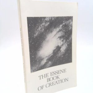 May include: A hardcover book titled "THE ESSENE BOOK OF CREATION" with a black and white image of a galaxy on the cover. The book is off-white and angled slightly to the left.