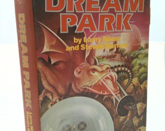 May include: A vintage paperback book titled "Dream Park" by Larry Niven and Steven Barnes. The cover features a red dragon, a futuristic scene, and the book's title in large, orange letters. The spine also displays the title and authors.