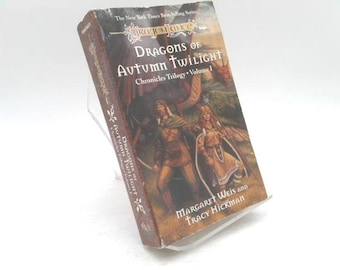 May include: A hardcover book titled "Dragons of Autumn Twilight" from the "Dragonlance" series. The cover features a fantasy illustration of two figures in medieval attire, with a dragon in the background. The author's names are Margaret Weis and Tracy Hickman.