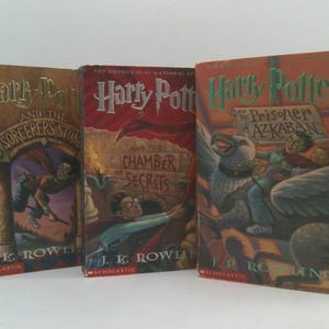 May include: Three hardcover books from the Harry Potter series. The book covers are in shades of brown, red, and orange, with illustrations of characters and scenes from the stories. Titles include "Harry Potter and the Sorcerer's Stone", "Harry Potter and the Chamber of Secrets", and "Harry Potter and the Prisoner of Azkaban".