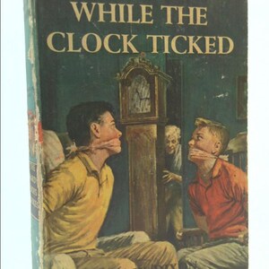 May include: The Hardy Boys book cover, "While the Clock Ticked" by Franklin W. Dix. The cover features a vintage illustration of two boys tied up with their mouths covered, a clock on the wall, and a woman peeking from behind a door.