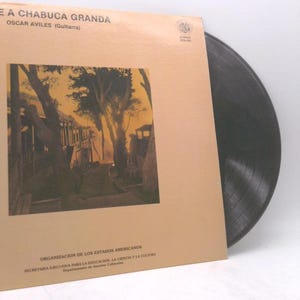 May include: A vintage vinyl record album titled "E A CHABUCA GRANDA" by Oscar Aviles. The album cover is tan with a sepia-toned image of a street scene. The record itself is black and partially visible.