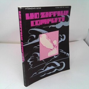 May include: A black guitar music book titled "Led Zeppelin Complete" with pink and white text. The cover features a pink square with a white and pink illustration, and stylized clouds. The spine is pink with white text.