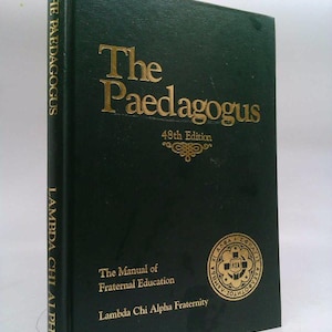 May include: A dark green book titled "The Paedagogus" with gold lettering. The book is the 48th edition and is subtitled "The Manual of Fraternal Education" by Lambda Chi Alpha Fraternity. The spine reads "The Paedagogus" and "Lambda Chi Alpha".
