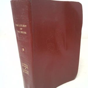 May include: A burgundy-colored book titled "The Liturgy of the Hours" with gold lettering. The book has a purple ribbon attached to the top. The spine reads "II", "Lenten Season", and "Easter Season".