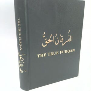 May include: A hardcover book titled "THE TRUE FURQAN" in gold lettering on a black cover. The book's spine also features the title in gold. The cover also has Arabic script. The book is standing upright.