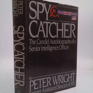 May include: A hardcover book titled "SPY CATCHER" by Peter Wright. The book has a black cover with white lettering and a red hammer and sickle symbol. The cover also features the flags of the United Kingdom and the United States.