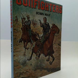 May include: A vintage paperback book cover with a colorful illustration of two cowboys on horseback in a gunfight. The title of the book is "Gunfighters" by Robin May.