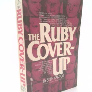 May include: The Ruby Cover-Up book cover features a pink background with the title in white and black text. The cover also features several black and white photos of men.