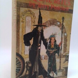 May include: A hardcover book titled "EQUAL RITES" by Terry Pratchett. The cover art features a witch in a black hat and cloak, a young person in a robe, and a small creature. The spine reads "EQUAL RITES".