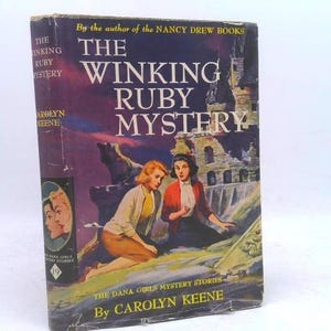 May include: A hardcover book titled The Winking Ruby Mystery by Carolyn Keene, part of the Dana Girls Mystery Stories series. The cover features an illustration of two individuals near a stone structure against a dark, purple-toned sky.