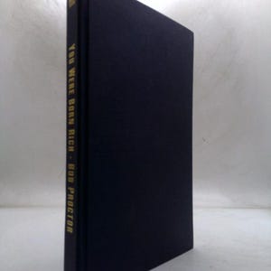 May include: A hardcover book titled "YOU WERE BORN RICH" by Bob Proctor. The book has a dark blue cover and spine. The title and author's name are printed in gold lettering on the spine. The book is standing upright against a white background.