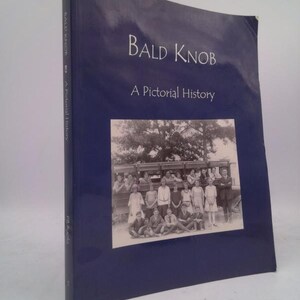 May include: A hardcover book titled "Bald Knob: A Pictorial History" with a dark blue cover. The book features a black and white photograph of a group of people. The spine of the book has the title and author's name.