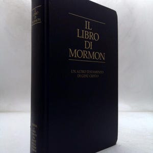May include: A hardcover book titled "IL LIBRO DI MORMON" in gold lettering on a dark blue cover. The spine also features text. The book is a religious text, with the subtitle "UN ALTRO TESTAMENTO DI GESÙ CRISTO".