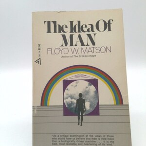 May include: A book cover with a rainbow arch and a silhouette of a person standing in a circle. The title of the book is "The Idea Of Man" by Floyd W. Matson. The book cover is a light beige color with black text. The quote "As a critical examination of the views of those who would have us believe that man is little more than a biologically driven machine... it is the best, most readable and heartening of its kind." -Ashley Montagu is printed at the bottom of the cover.
