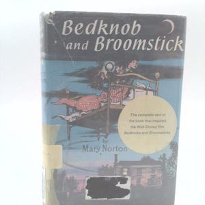 May include: A hardcover book titled "Bedknob and Broomstick" by Mary Norton. The cover features an illustration of a bed flying through the air, with a crescent moon in the upper right corner. The book is the complete text that inspired the Walt Disney film.