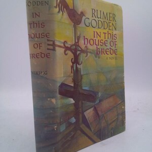 May include: A vintage hardcover book titled "In This House of Brede" by Rumer Godden. The cover features a painting of a cross, a weather vane, and a church. The book is published by Viking.
