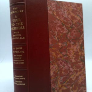 May include: A hardcover book titled "The Journal of a Tour to the Hebrides" with a maroon cover and marbled design. The spine features gold lettering and the author's name. The book is a vintage edition from The Limited Editions Club.