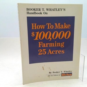 May include: A book titled "Booker T. Whatley's Handbook On How To Make $100,000 Farming 25 Acres." The cover features text in orange and white on a navy blue background. The book is beige with a clear plastic stand.