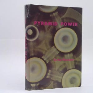 May include: A hardcover book titled Pyramid Power by G. Max Toth with a dark brown cover featuring a repeating pattern of yellow and white circular shapes. The title and author name are printed in bright pink text on the front cover.