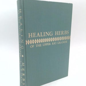May include: A hardbound book with a muted green cover featuring gold lettering that reads HEALING HERBS OF THE UPPER RIO GRANDE. The title is centered above a decorative geometric triangle pattern, with the title repeated vertically on the spine.