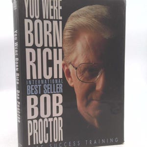 May include: A hardcover book titled "YOU WERE BORN RICH" by Bob Proctor. The cover features a portrait of a man wearing glasses and the text "INTERNATIONAL BEST SELLER". The spine reads "YOU WERE BORN RICH - BOB PROCTOR".