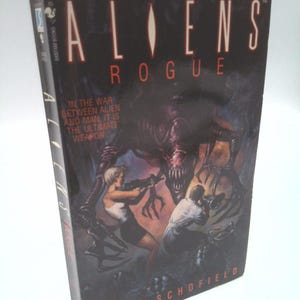 May include: A paperback book titled "ALIENS ROGUE" with a dark cover featuring a menacing alien creature and two figures with weapons. The text reads "IN THE WAR BETWEEN ALIEN AND MAN, IT IS THE ULTIMATE WEAPON."
