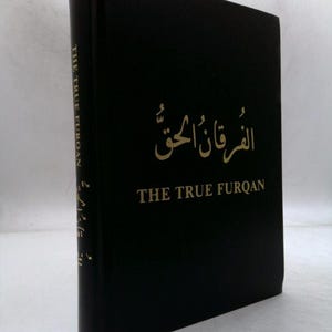 May include: A black hardcover book titled "THE TRUE FURQAN" in gold lettering. The book's title is also written in Arabic script. The spine of the book also has text in gold. The book is standing upright.