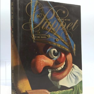May include: The Art of the Puppet book cover features a colorful puppet with a large nose, one eye, and a blue hat with gold trim. The title "The Art of the Puppet" is written in gold script.