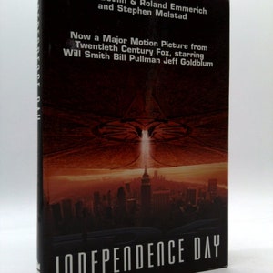 May include: Book cover for the novel "Independence Day" by Dean Devlin, Roland Emmerich, and Stephen Molstad. The cover features a dramatic image of a large alien spacecraft hovering over a city skyline.
