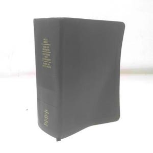 May include: A dark gray book with gold lettering. The book's spine displays the title "Holy Bible" and other religious texts. The book is standing upright on a white surface.