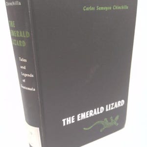 May include: A hardcover book titled "The Emerald Lizard" by Carlos Samayoa Chinchilla. The book has a black cover with white and green text and a green lizard illustration. The spine reads "Tales and Legends of Guatemala".