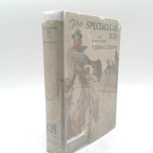 May include: A vintage book titled "The Spectacular Kid" by Robert J. Horton. The cover features an illustration of a person in Western attire, holding a hat. The book has a tan cover with white text and a white spine.