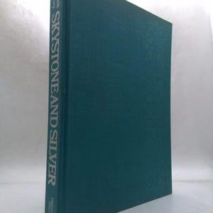 May include: A teal hardcover book titled "Skystone and Silver" by Roniek Stacey. The book's spine displays the title in silver lettering, with the publisher's name at the bottom. The cover has a subtle embossed pattern.
