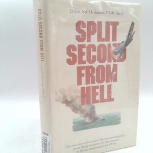 May include: A hardcover book titled Split Second From Hell by Lt. Col. Jack McGuckin, USMC (Ret.). The off-white cover features bold red text, an illustration of a military aircraft, and a plume of smoke over water. A barcode sticker is on the spine.