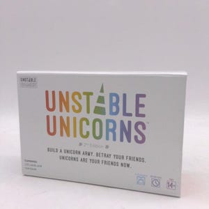 May include: A white box for the game "Unstable Unicorns" with colorful text. The game's title is in rainbow colors. The box includes text that says "Build a unicorn army. Betray your friends. Unicorns are your friends now."