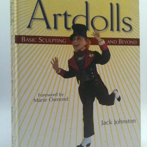 May include: Book cover with a yellow and white striped background. The title is "Artdolls: Basic Sculpting and Beyond". The cover features a whimsical doll wearing a black top hat, a red vest, and black pants. The text "Foreword by Marie Osmond" and "Jack Johnston" are also visible.