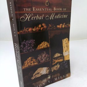 May include: A hardcover book titled The Essential Book of Herbal Medicine by Simon Y. Mills. The dark brown cover features a photograph of wooden shelves filled with various dried herbs, roots, and flowers, with the author's name at the bottom.