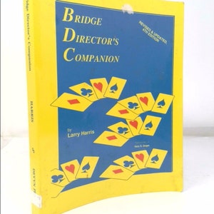May include: A yellow book titled "Bridge Director's Companion" with a blue background and playing cards. The book is by Larry Harris and is revised and updated for the 4th edition.